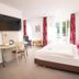 Haus Dumicketal in Drolshagen: bright hotel room with double bed, desk, wall-mounted TV and balcony doors