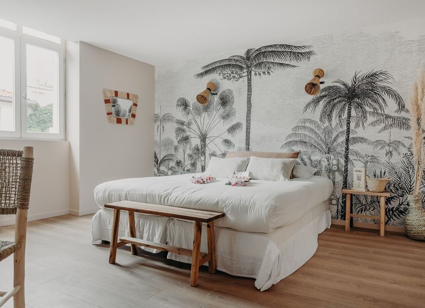 Palmito in Biarritz bedroom with palm-tree mural, white bed, and wood bench