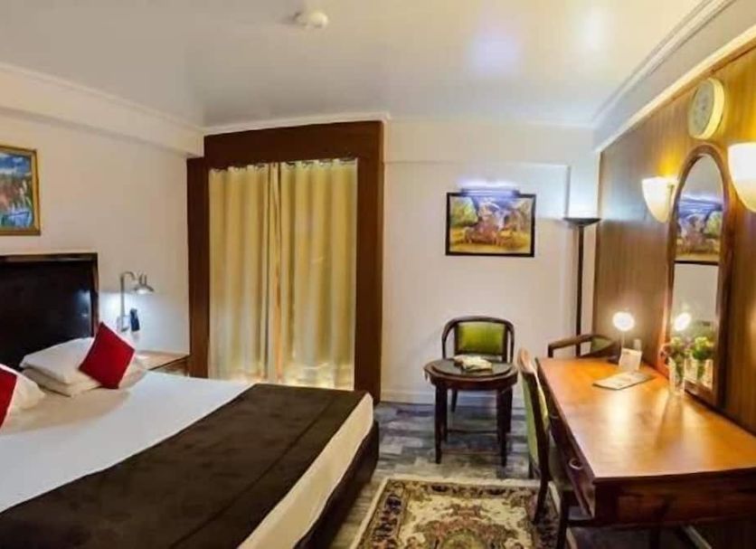 Hotel Galaxy Karachi guest room with king bed, desk, mirror and window curtains