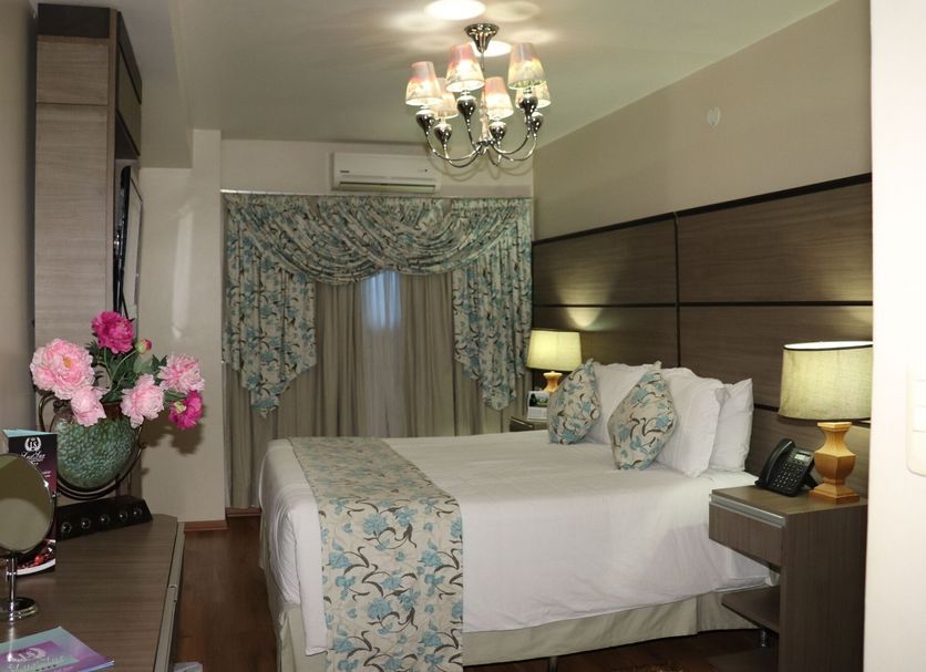 Luxsur Encarnación guest room with king bed, bedside lamps, chandelier and floral curtains