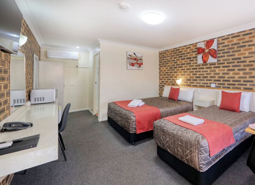 Top Of The Town Motel Inverell room with two beds, desk and brick accent wall