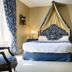 Domaine De Brou in Noyant-de-Touraine bedroom with blue canopy bed, patterned curtains and armchairs