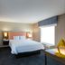 Hampton Inn and Suites Jamestown guest room with king bed, bathroom doorway, and window seating area