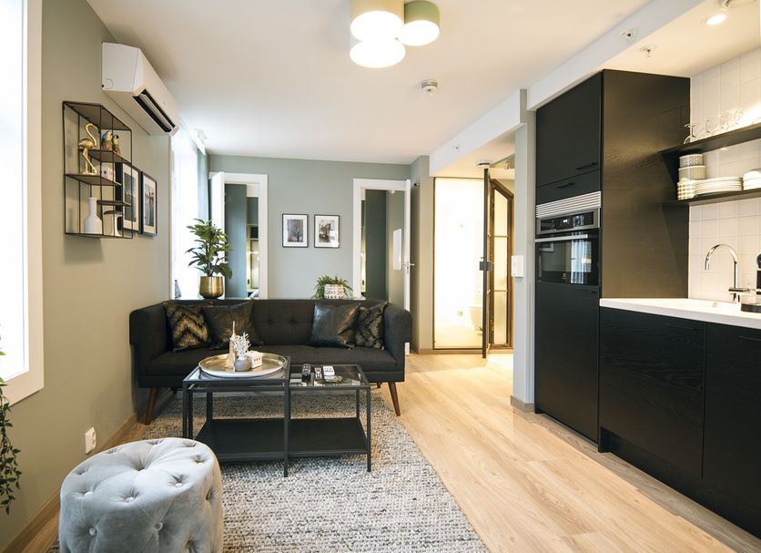 Home Again Apartments Nygata 1 in Stavanger: modern apartment living area with black sofa, kitchenette, and dining space.