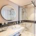 Golden Tulip Aix Les Bains bathroom with round mirror, vessel sink and glass walk-in shower