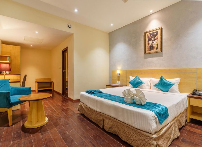 The Platinum Hotel in Hyderabad guest room with king bed, teal chairs, and small seating area