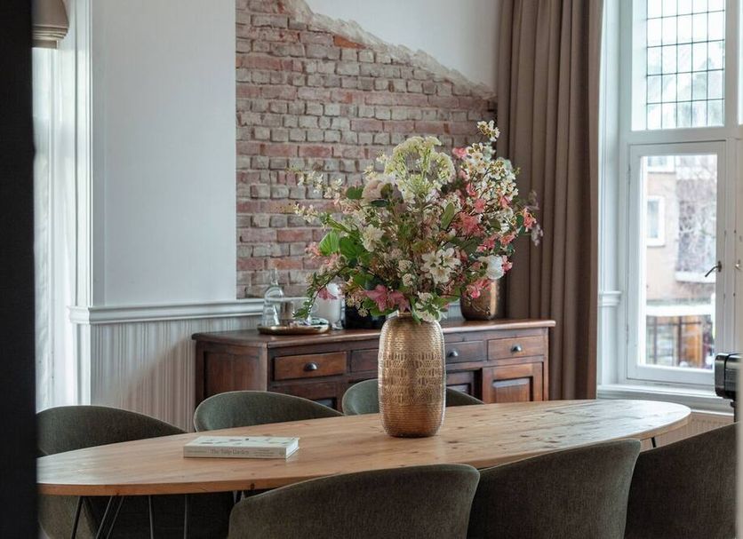 Hotel Het Oude Raadhuis dining room with brick accent wall, wooden table, and flower vase in Castricum