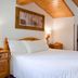 Hotel Scoiattolo in Falcade bedroom with wooden bed, sloped wood ceiling and twin beds by window.