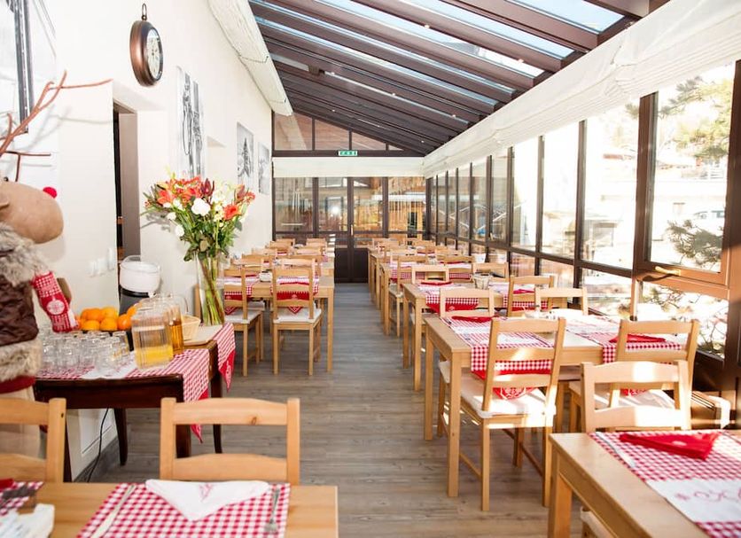Hotel Bristol Verbier in Bagnes, glass-roofed dining room with wooden tables and red checkered tablecloths