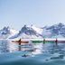 Kayakers on calm water with snowy mountains at Nusfjord Village & Resort, Ramberg