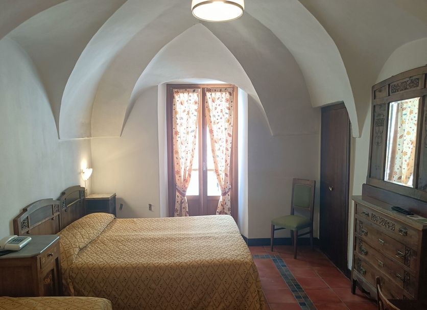 Hotel Gufo in Bormio room with vaulted ceiling, bed, dresser and window with curtains