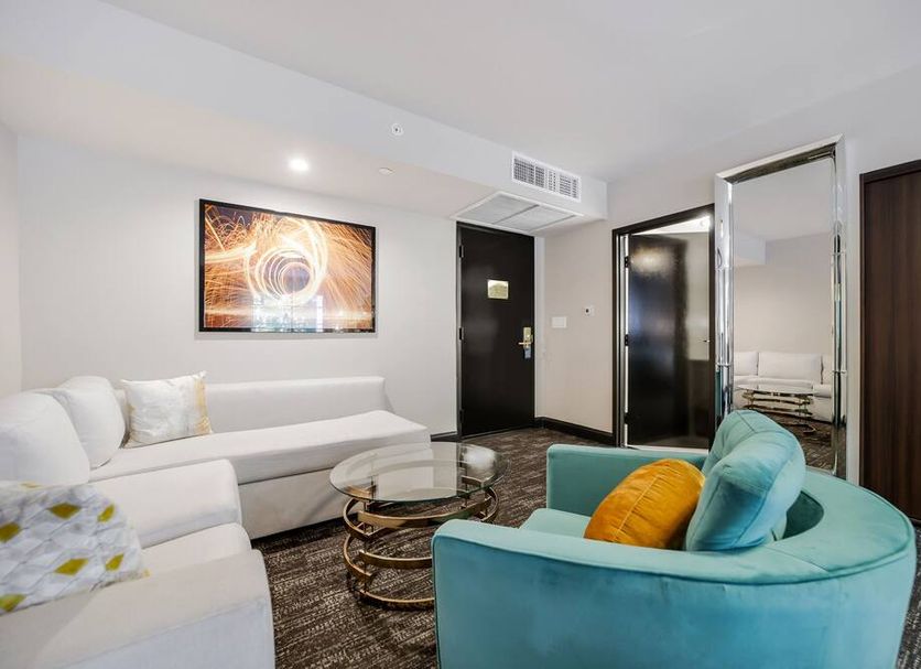 Venezia in Miami Beach hotel room with white sectional sofa, teal chair, glass tables, and mirror wall