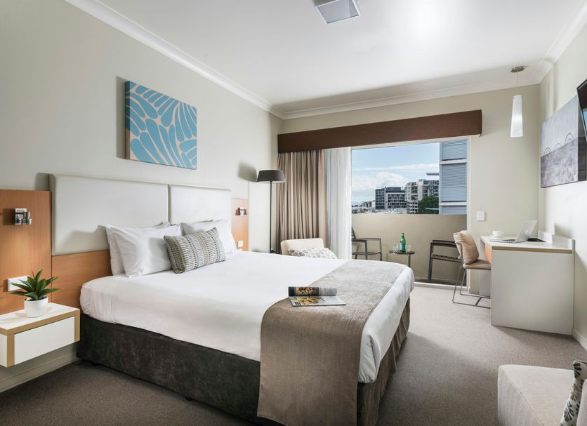 Grand Hotel and Apartments Townsville bedroom with king bed, desk, and balcony city view in Townsville