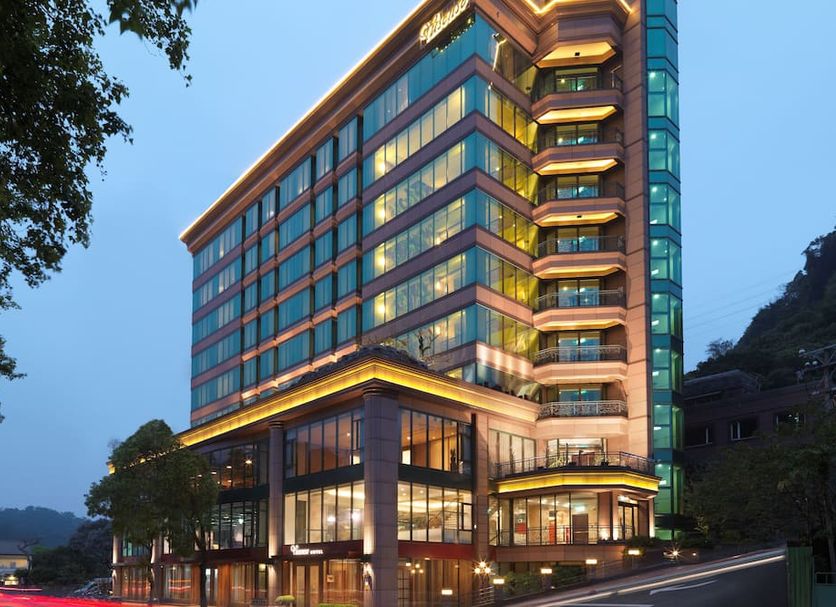 Yusense Hotel in Taipei City at dusk, showing a modern glass facade and illuminated exterior