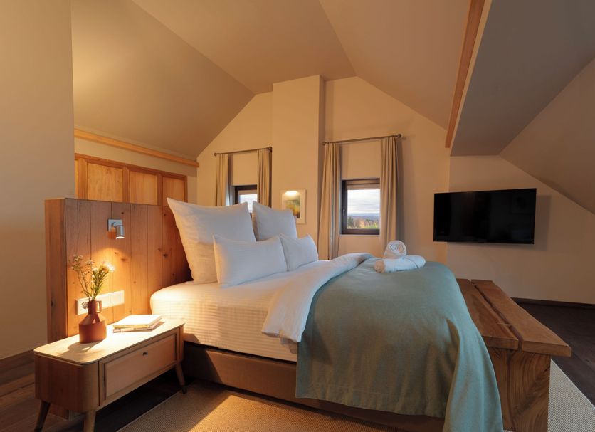 Hochblauen Hotel in Badenweiler, cozy attic room with king bed, bedside table, and wall-mounted TV