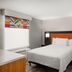 Home2 Suites by Hilton Alexandria guest room with queen bed, colorful window valance, and patterned carpet