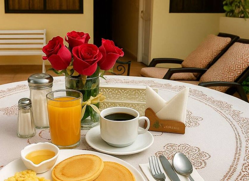 La Rosario Hostal Quito breakfast tray with coffee, juice, pancakes and red roses on a table