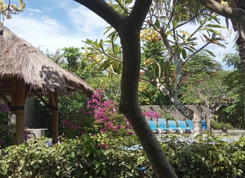 Vico Hotel, South Kuta: tropical garden with thatched gazebo, lounge chairs and flowering shrubs