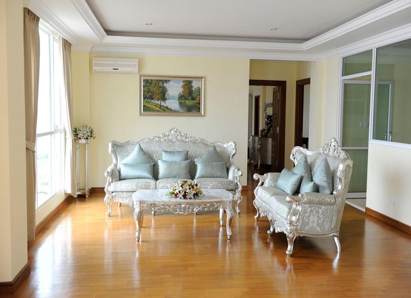 Mawlamyine Strand Hotel lounge in Mawlamyine with ornate sofas, coffee table, wood floor, and large windows