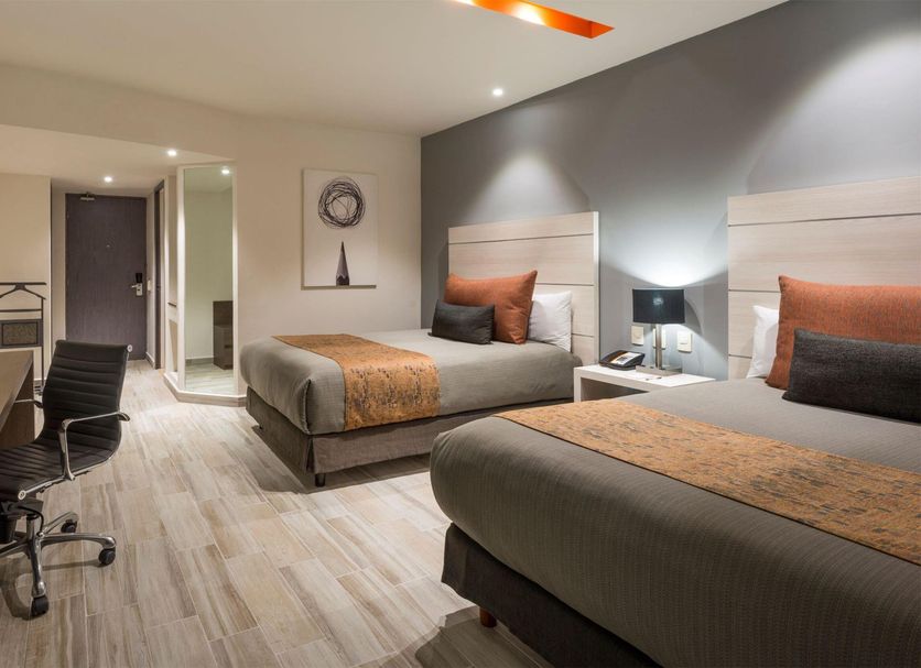 Real Inn Perinorte in Tlalnepantla guest room with two beds, desk, wall-mounted TV and modern seating area