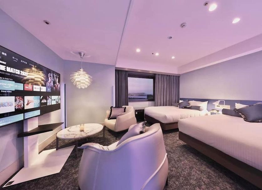 Minamisenri Crystal Hotel in Suita guest room with two beds, lounge chairs and a city view