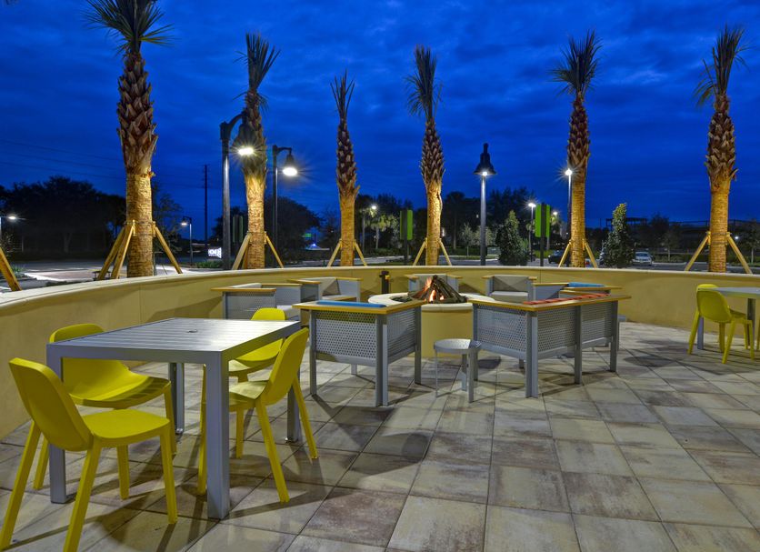 Home2 Suites by Hilton Orlando at FLAMINGO CROSSINGS Town Center patio with tables and yellow chairs at dusk