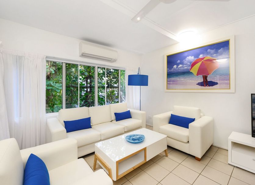 By The Sea Port Douglas living room with white sofas, blue accents, and tropical garden view