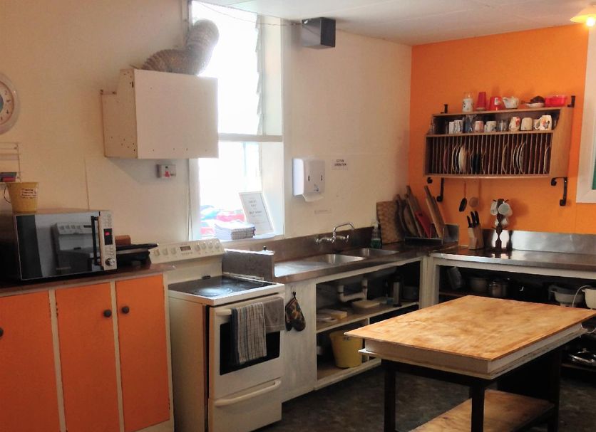 Abel's Central Backpackers kitchen in Nelson with orange cabinets, stove, sink and prep tables