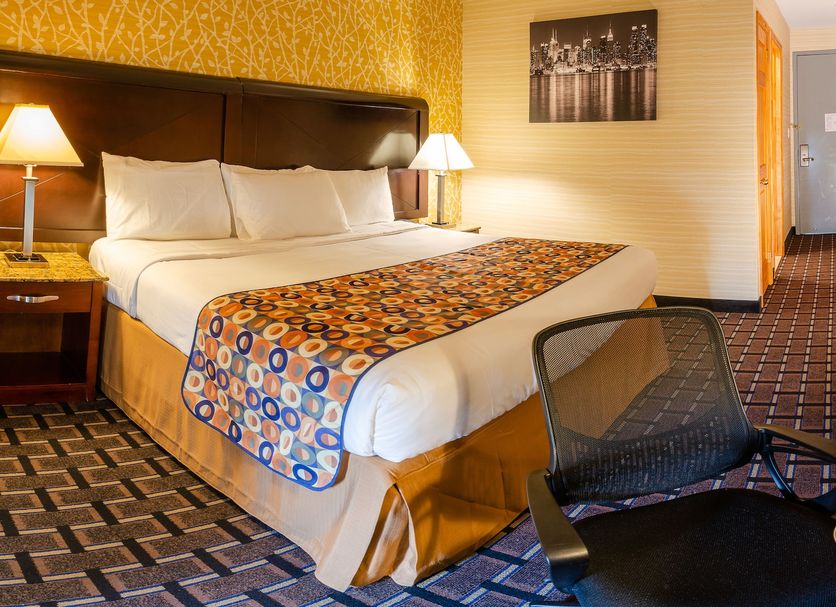 Elmhurst Hotel in Queens room with king bed, bedside lamps, desk chair and patterned carpet