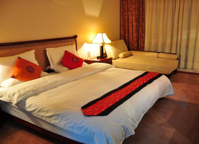 Lijiang Liwang Hotel in Lijiang guest room with king bed, chaise lounge, and bedside lamp