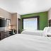 Holiday Inn Express & Suites Ada By IHG guest room with two beds, wall-mounted TV, desk and green accent wall