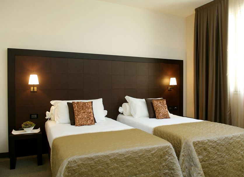Sweet Hotel in Schiavon: twin beds with beige bedding, bedside lamps and tall curtains in a simple guest room