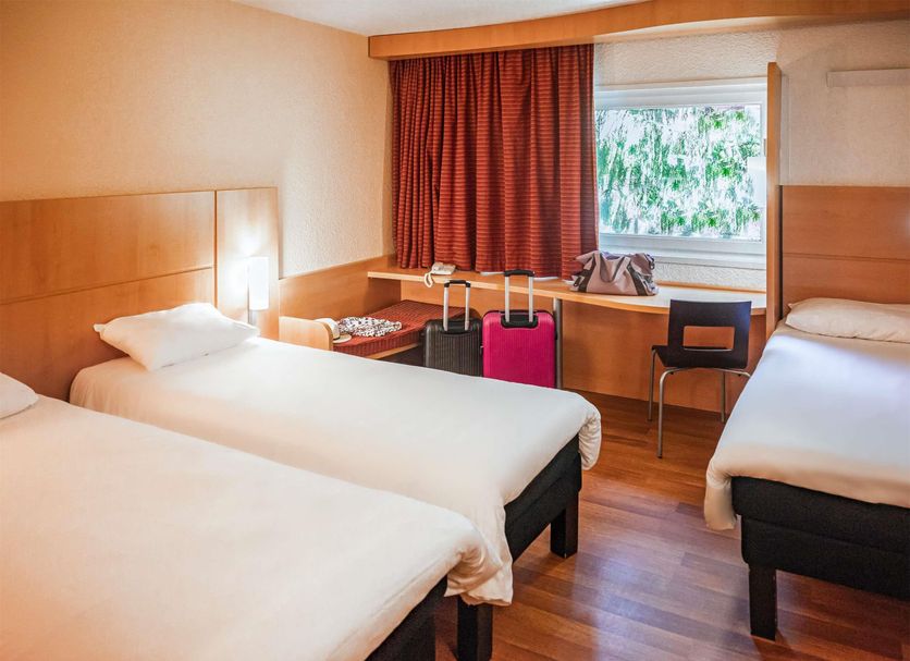 ibis Belfort Danjoutin room with three single beds, window and luggage on desk