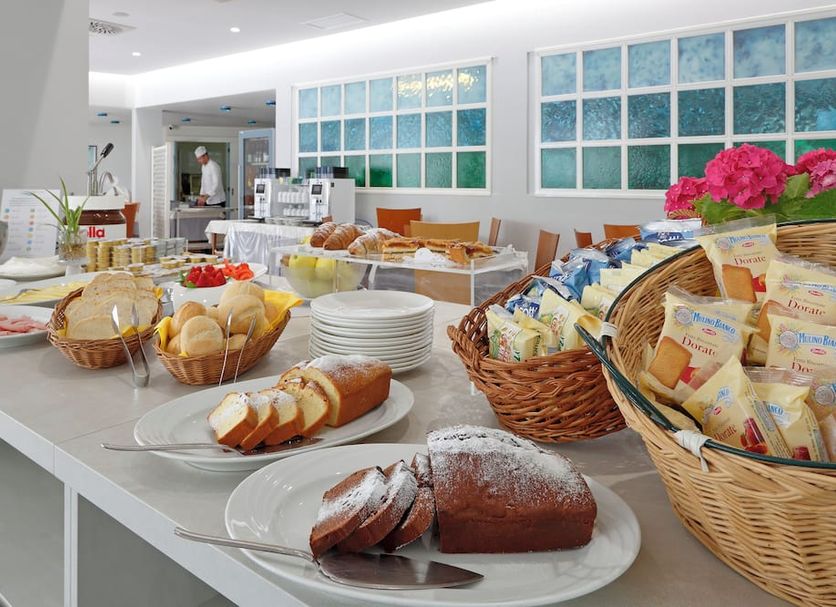 Breakfast buffet at Hotel Smeraldo in Lignano Sabbiadoro with pastries, bread, fruit and baskets of packaged snacks.