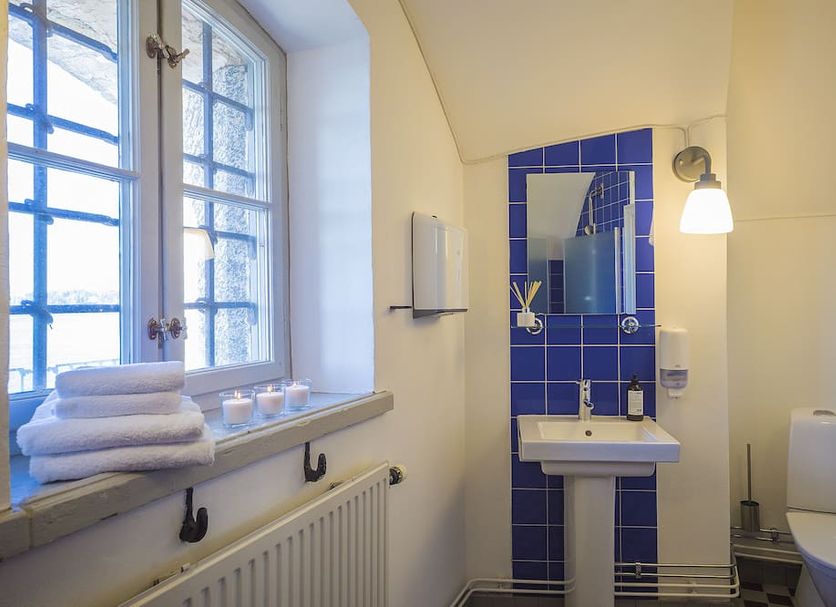 Kastellet Bed & Breakfast, Vaxholm: compact bathroom with sink, toilet, blue tile shower, and window