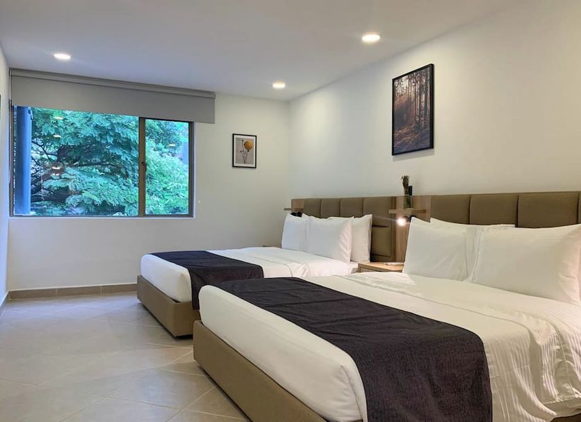 Hotel Poblado Boutique in Medellín guest room with two beds and a large window view of greenery