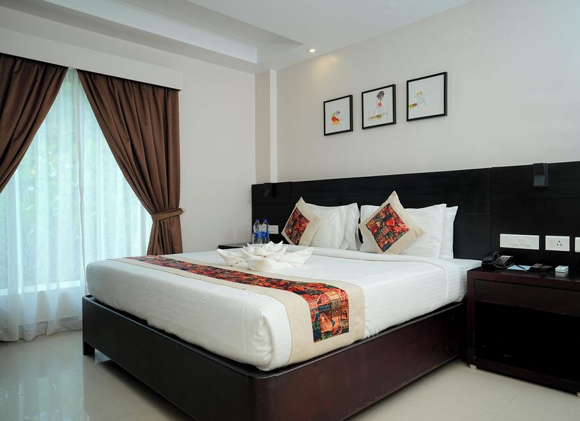 Dfort Hotel Kollam room with a king bed, bedside table, framed wall art and sheer curtains in Kollam
