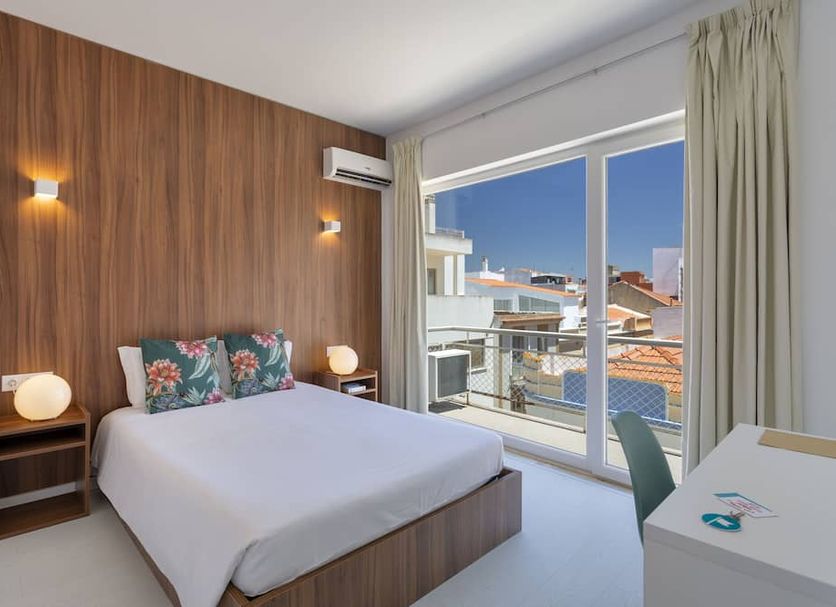 Next Inn Portimão guest room with bed, wood accent wall and balcony doors overlooking rooftops
