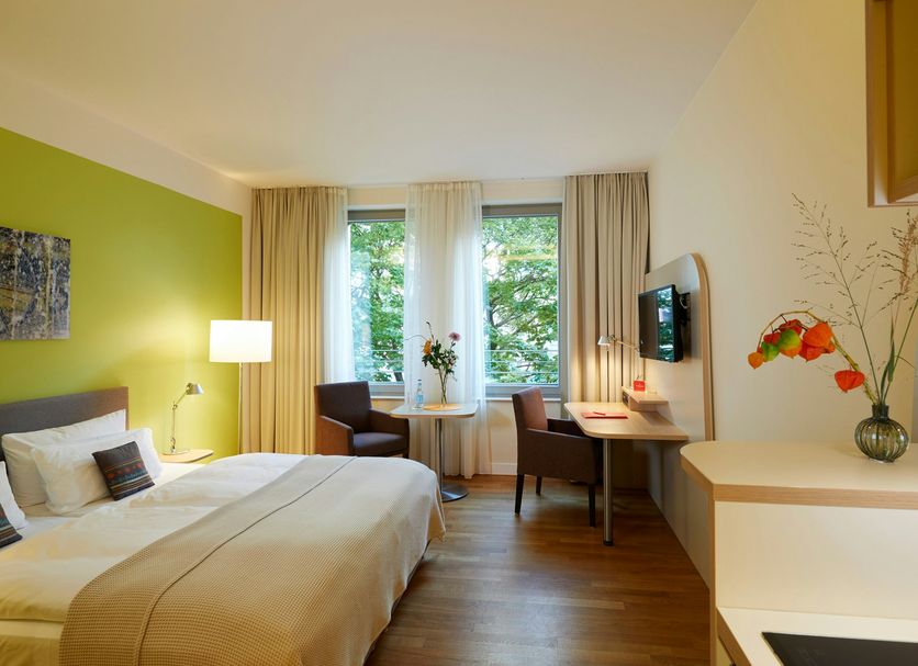 Flottwell Berlin Hotel guest room with bed, desk, chairs, and large windows in Berlin