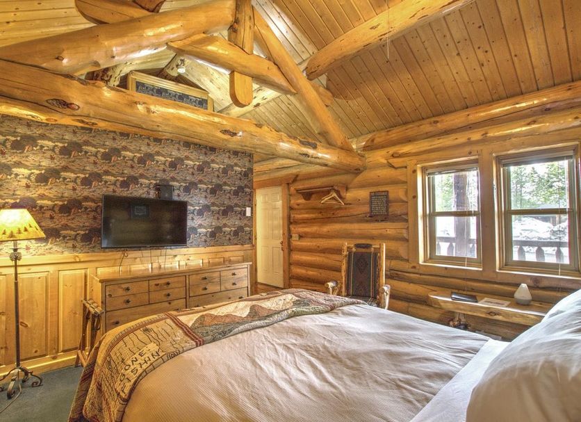 Hibernation Station in West Yellowstone log cabin guest room with TV, stone fireplace, and wood-beam ceiling