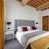 Relais Villa Grazianella Una Esperienze bedroom in Acquaviva with tufted bed, yellow bench and wood beams