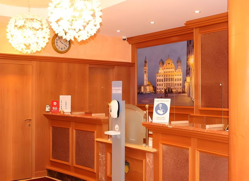 Stadthotel Augsburg reception area with wood-paneled front desk and warm pendant lights in Augsburg