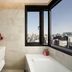 Moxy Seoul Insadong bathroom with a soaking tub and city skyline view through corner windows