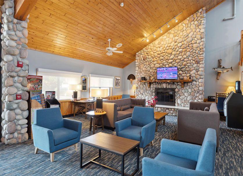 AmericInn by Wyndham Wisconsin Dells lobby with stone fireplace, wood ceiling, and blue seating