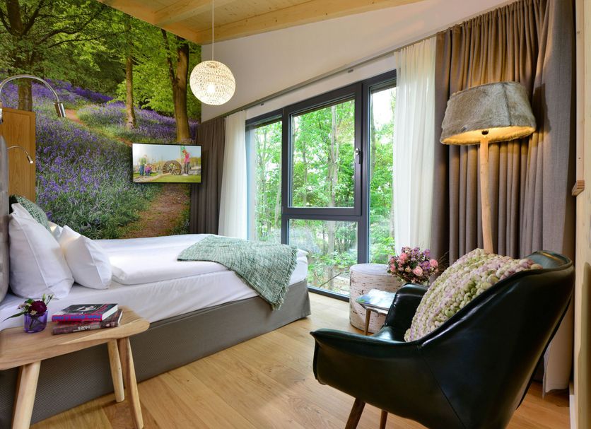 Hotel Fire & Ice Düsseldorf/Neuss room with bed, forest mural, floor lamp and green balcony view in Neuss