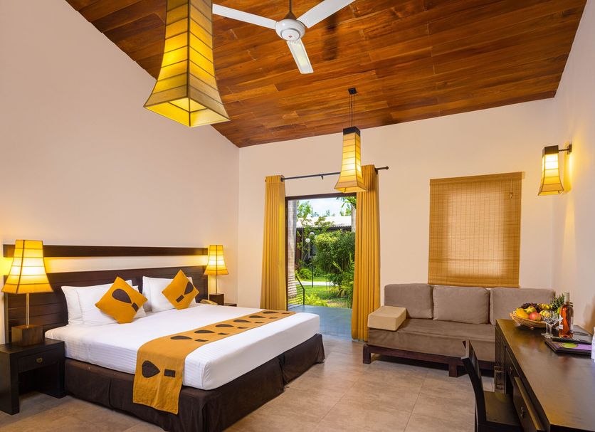 Chaarya Resort & Spa in Tissamaharama room with king bed, sofa, and garden view through open door