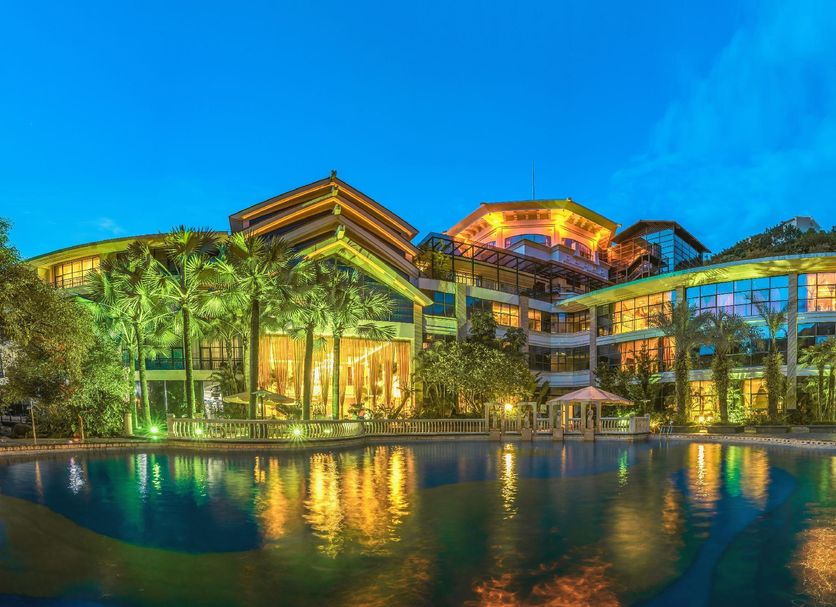 Hakka park International Hotel in Meizhou with lit exterior, palm trees, and reflection pool at dusk