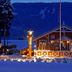 Hafjell Hotell in Øyer (Hafjell) lit up in snow with a red chalet and mountain backdrop