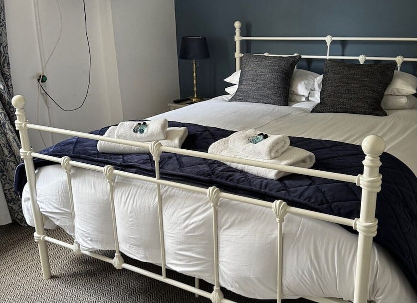 The Green Man, Rugby: white metal bed with dark bedding and folded towels in a guest room