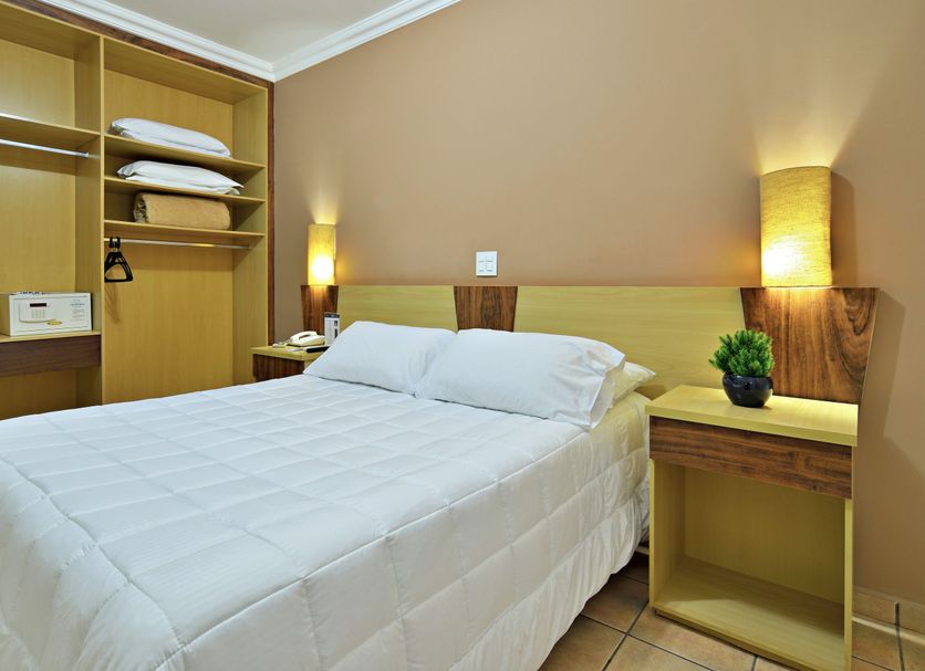 Plaza Inn Flat Araxá bedroom with double bed, bedside lamps and open closet in Araxá